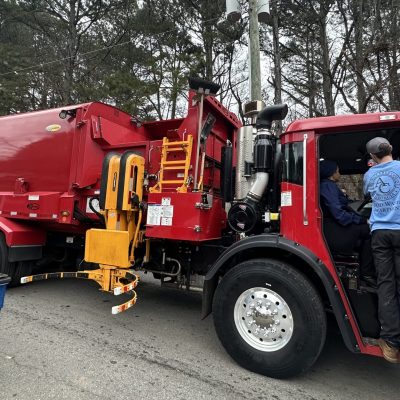 A person inspecting a red fire truck outdoors among trees.